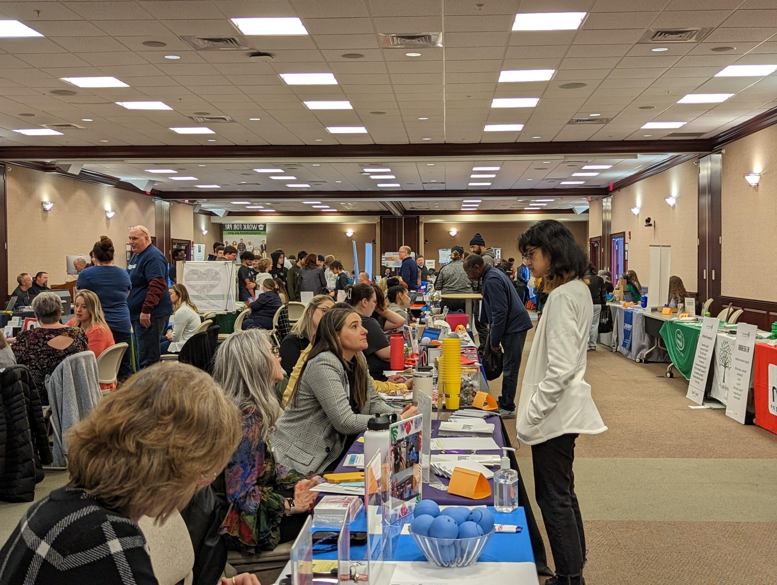 Image shows a student speaking to many employers sitting at tables in the CSC.